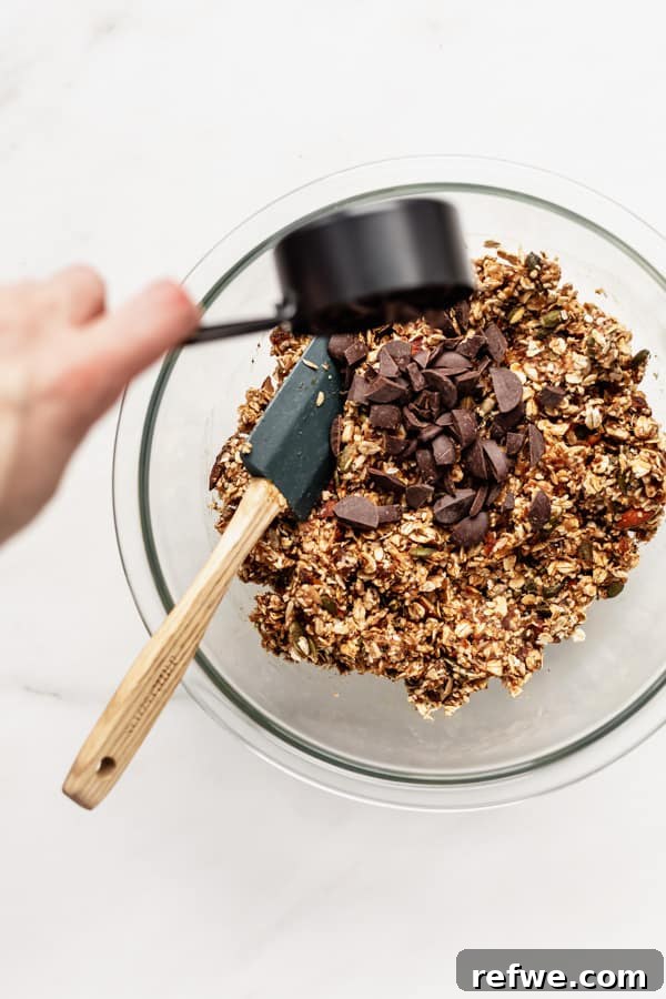 Supercharged Granola Fuel 7 a hand pouring chocolate chunks into a bowl of superfood granola bars ingredients