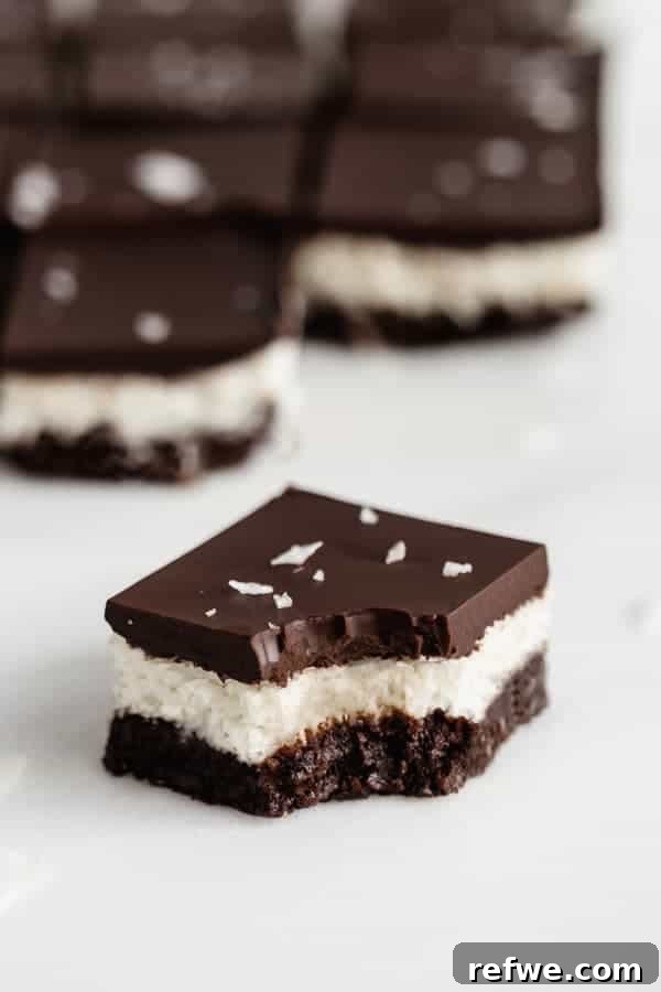 A no-bake chocolate coconut brownie with a bite taken out, showing the distinct layers.