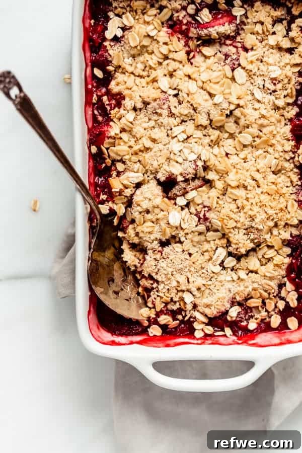 A healthy strawberry rhubarb crisp baked in a dish, with a serving spoon nestled in the juicy fruit and crumbly topping.