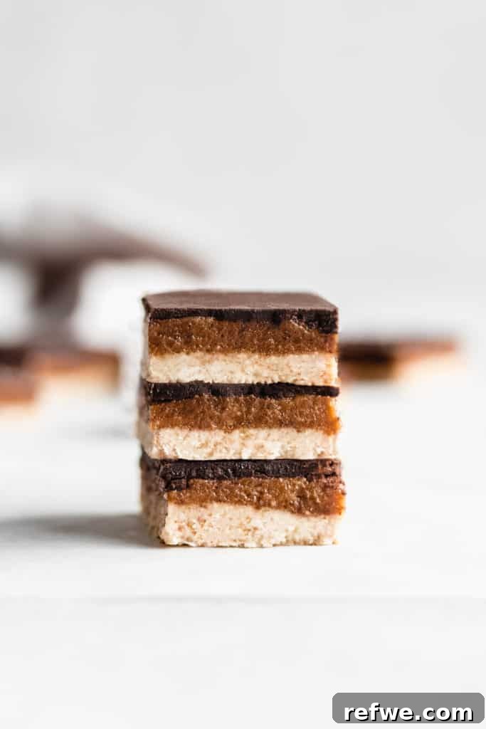 A stack of three raw salted caramel slices, showcasing distinct layers of base, caramel, and chocolate.