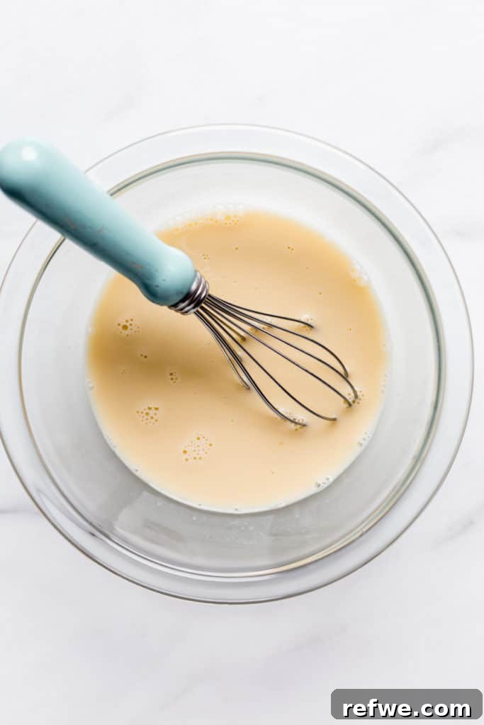 whisked eggs and coconut milk in a clear bowl with a small whisk in it
