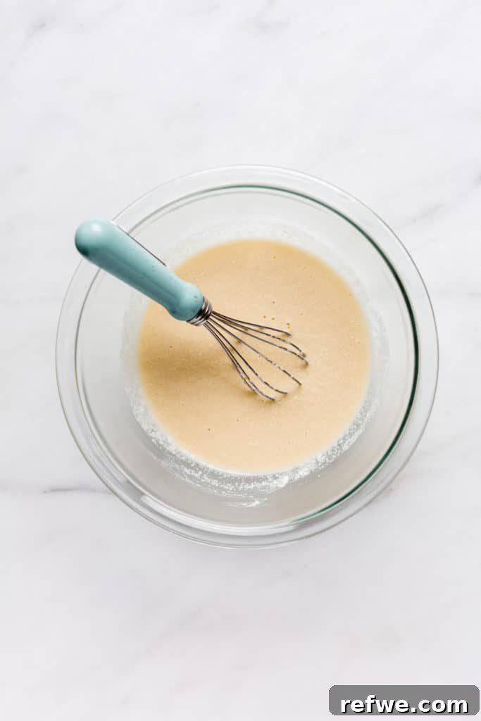 a clear mixing bowl with coconut flour pancake batter and a whisk in it