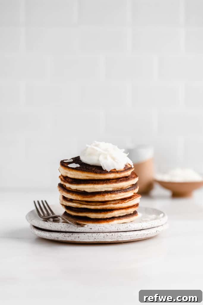 a stack of coconut flour pancakes on a white speckled plate with a fork on the side