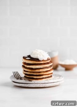 a stack of coconut flour pancakes on a white speckled plate with a fork on the side