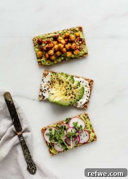 Three Ryvita crispbreads topped with avocado and various delicious toppings, with a napkin and knife on the side, ready to be served.
