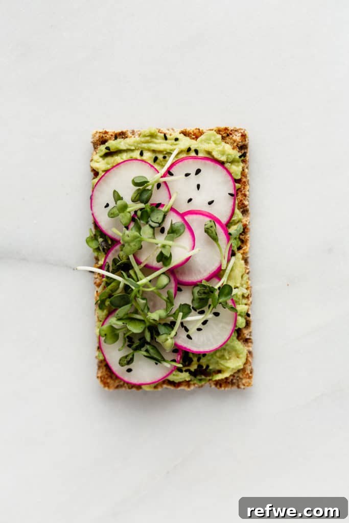 Avocado Toast: Three Creative Twists 6 A crisp Ryvita cracker base showcasing a vibrant topping of mashed avocado, thinly sliced radishes, and delicate radish sprouts, presenting a fresh and peppery flavor profile.