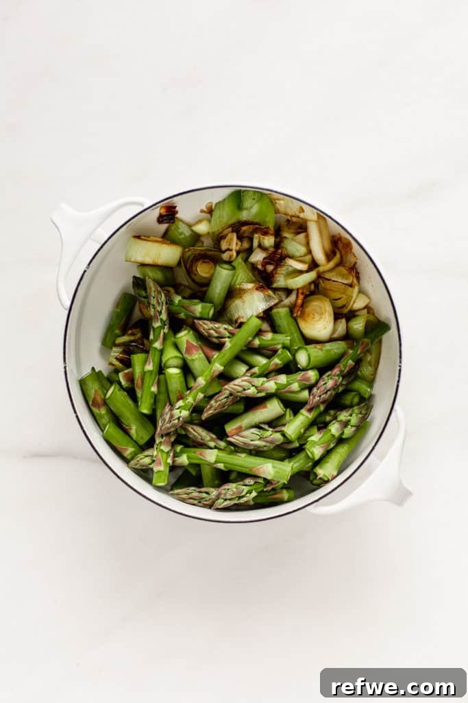 Leeks and asparagus cooking together in a white pot, releasing their flavors.
