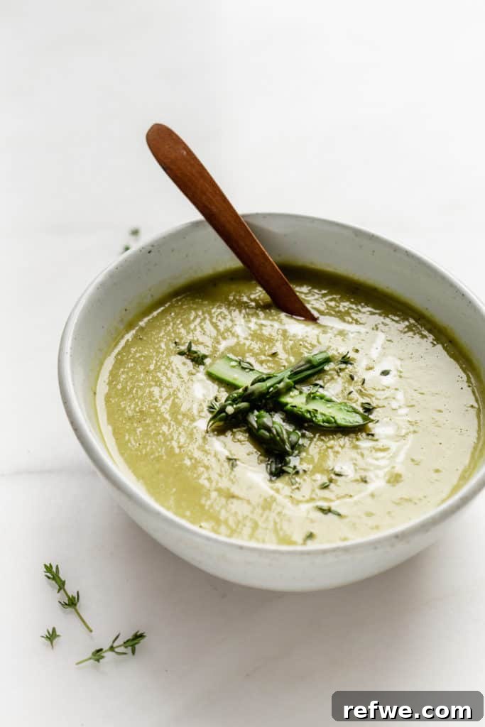 A serving bowl of creamy asparagus soup with a wooden spoon, ready to be enjoyed.