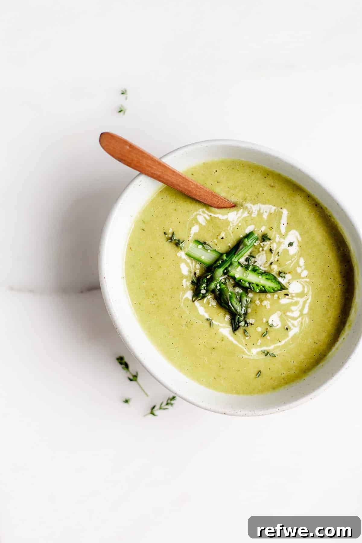 A beautifully presented bowl of vegan asparagus soup, garnished with freshly chopped asparagus and a swirl of cashew cream.