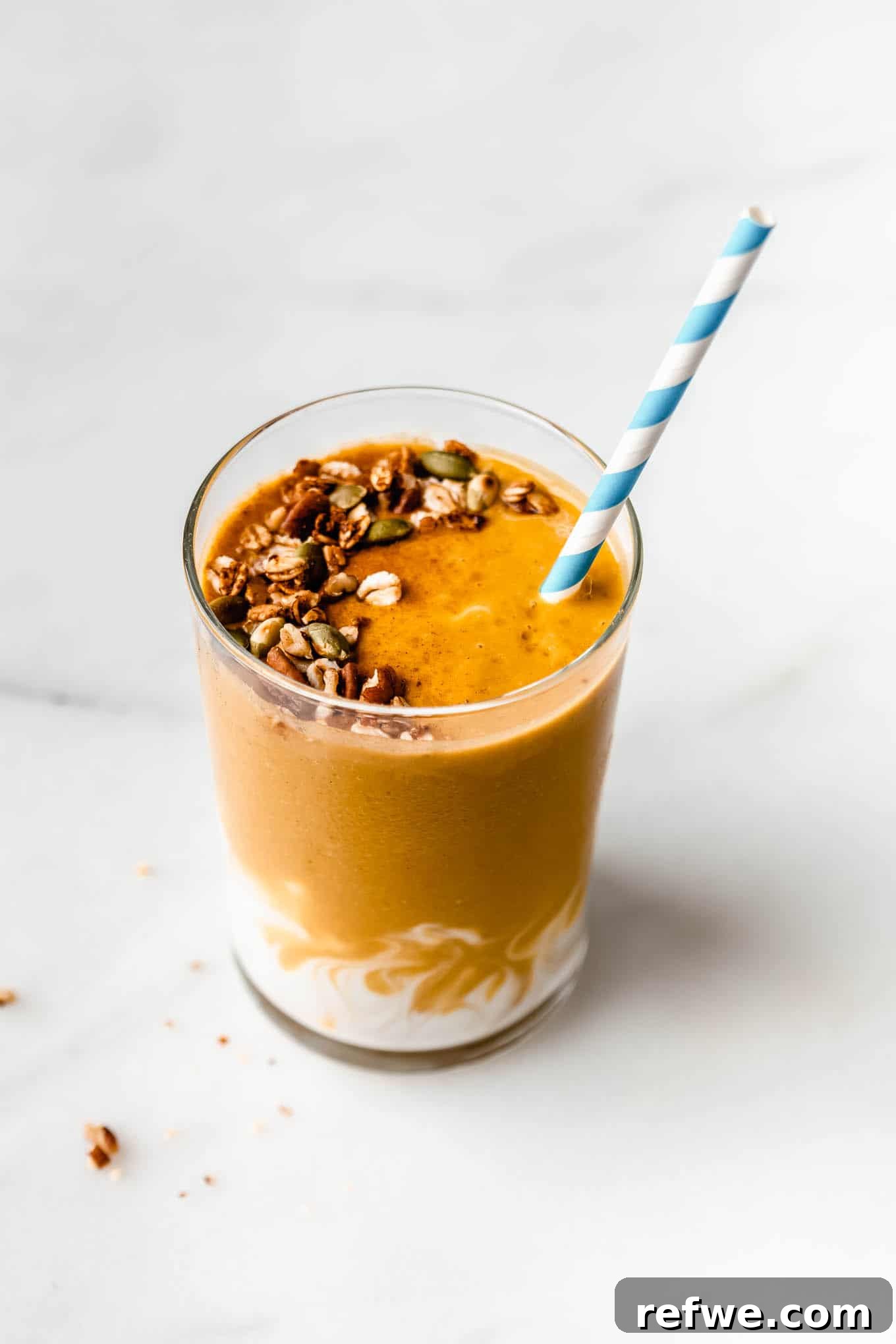 23 Simple Wholesome Morning Smoothies 16 a pumpkin pie smoothie topped with granola with a striped blue and white straw in it