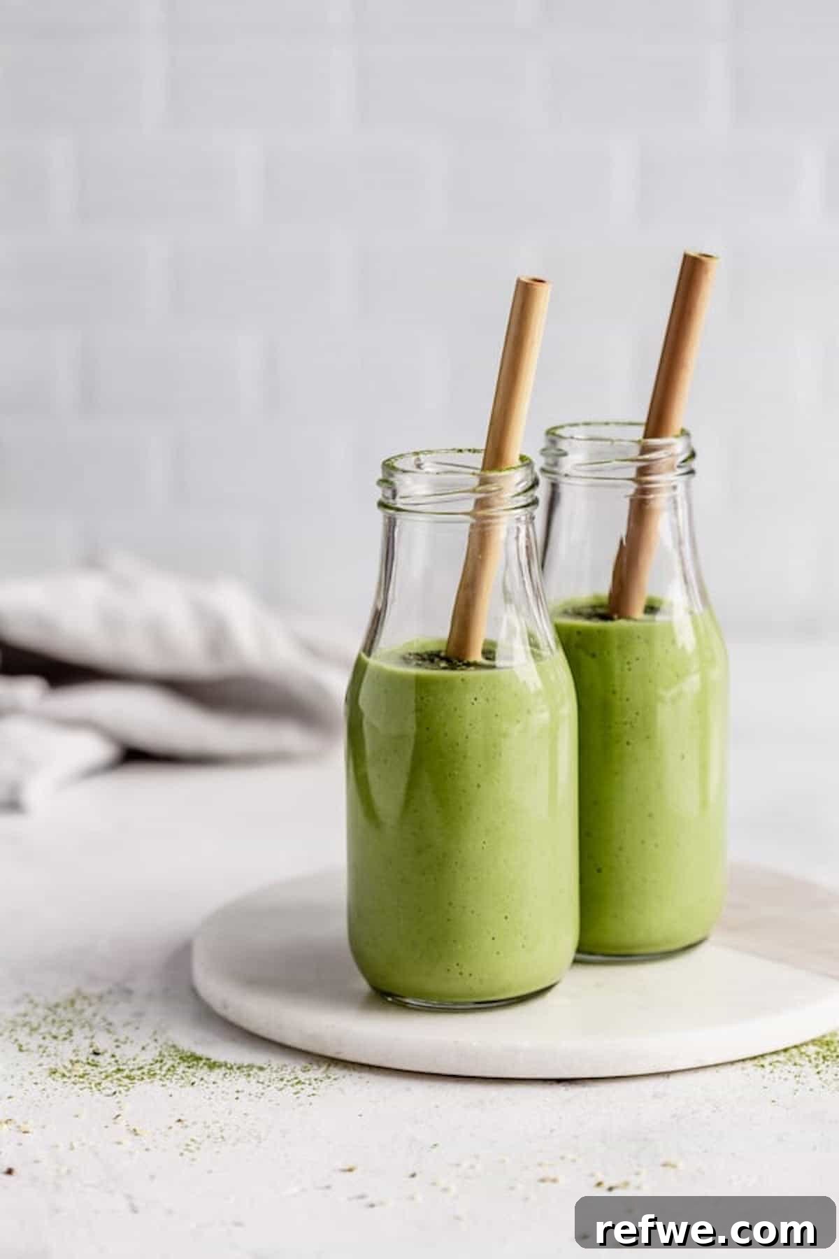23 Simple Wholesome Morning Smoothies 20 two brown paper straws sticking out of two tall glasses of matcha green tea smoothie on top of a marble serving platter against a white backdrop, healthy smoothie