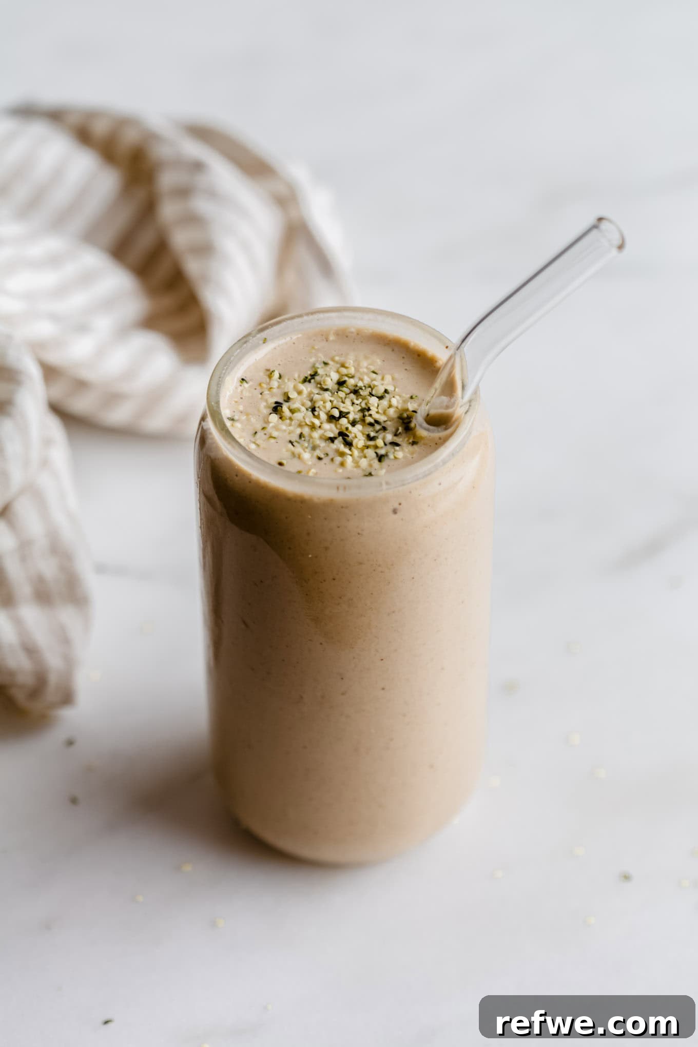 23 Simple Wholesome Morning Smoothies 3 A banana date smoothie in a glass topped with hemp seeds and a striped beige napkin on the side.