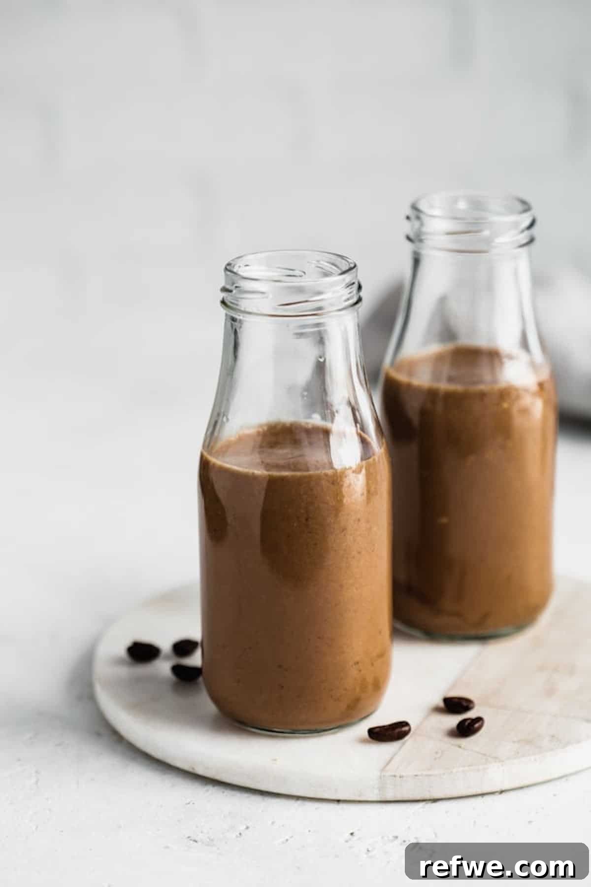 23 Simple Wholesome Morning Smoothies 5 two milk jars filled with coffee smoothie on a serving board with fresh whole coffee beans