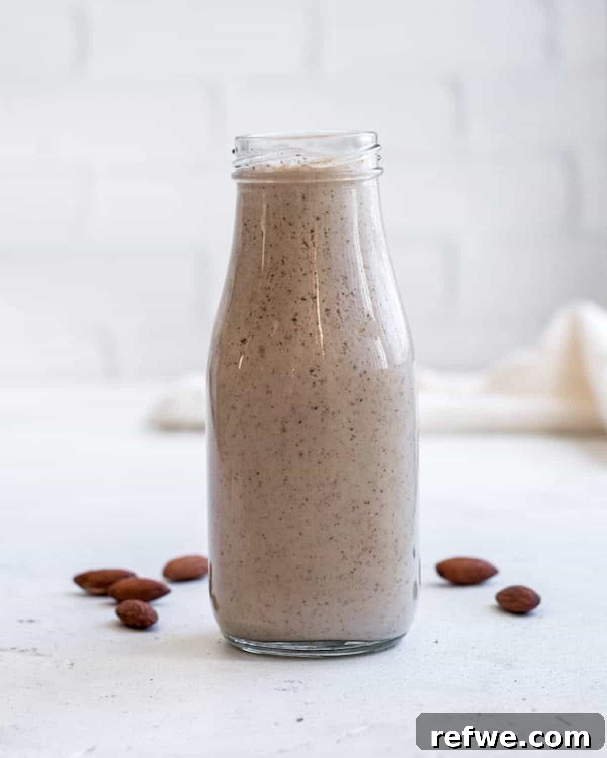23 Simple Wholesome Morning Smoothies 8 one brown speckled smoothie in a milk jar surrounded by whole almonds on a white background