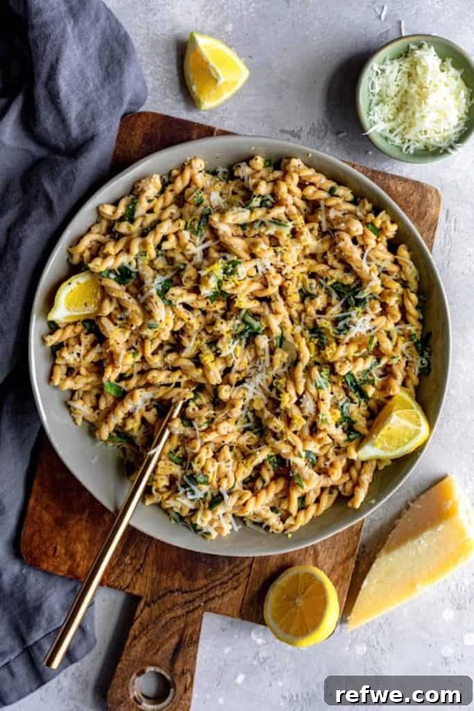 twisted pasta noodles covered in lemon basil sauce with shredded asiago cheese and lemon slices on a grey backdrop, summer salads with lemon wedges
