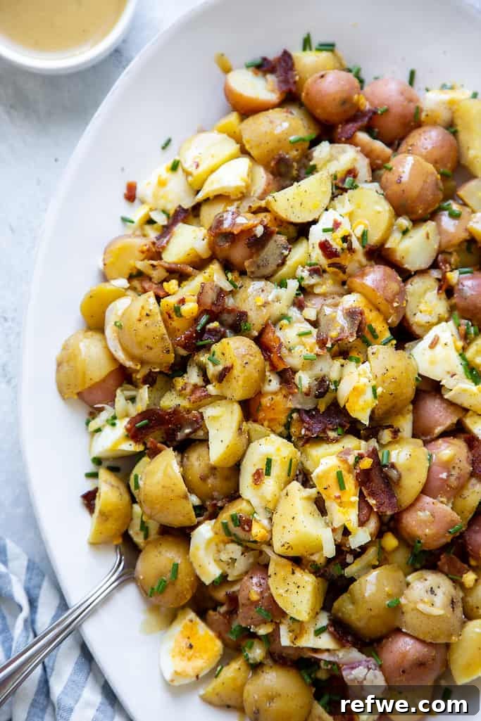 honey dijon potato salad mixed with boiled eggs, bacon, chives, and a honey mustard dressing on a white serving platter