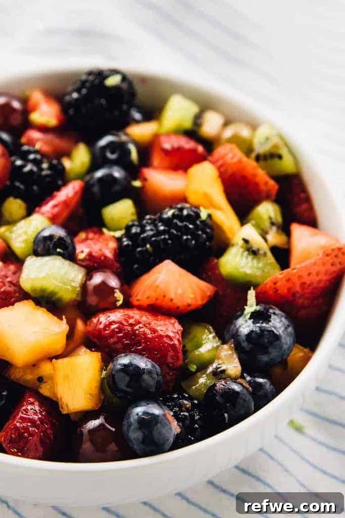 white bowl of fruity summer salads of blackberries, strawberries, kiwi, and mango against a white and blue striped linen