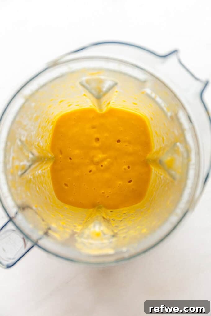 Freshly blended mango puree with coconut milk, maple syrup, and vanilla extract in a blender jar.