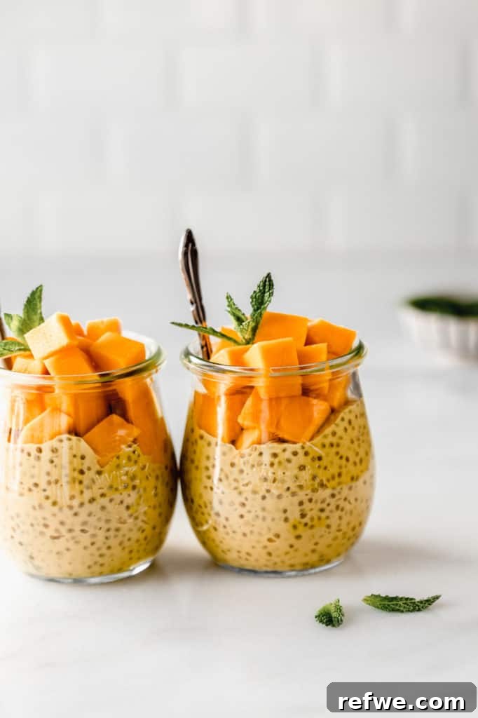 Two small glass jars filled with set mango chia pudding, elegantly topped with fresh mango cubes and a sprig of mint, ready for serving.