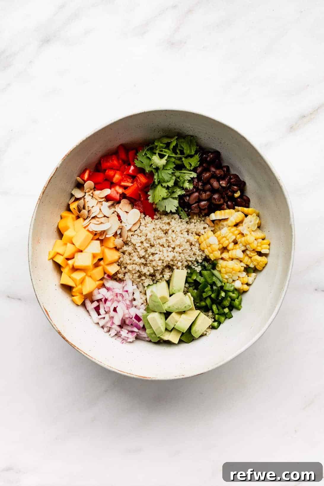 Zesty Southwestern Quinoa Power Bowl 3 A large mixing bowl filled with freshly cooked quinoa, colorful black beans, sweet corn, creamy avocado, spicy jalapeño, crisp red onions, juicy mango, crunchy almonds, vibrant red pepper, and fragrant cilantro, all ready to be tossed.