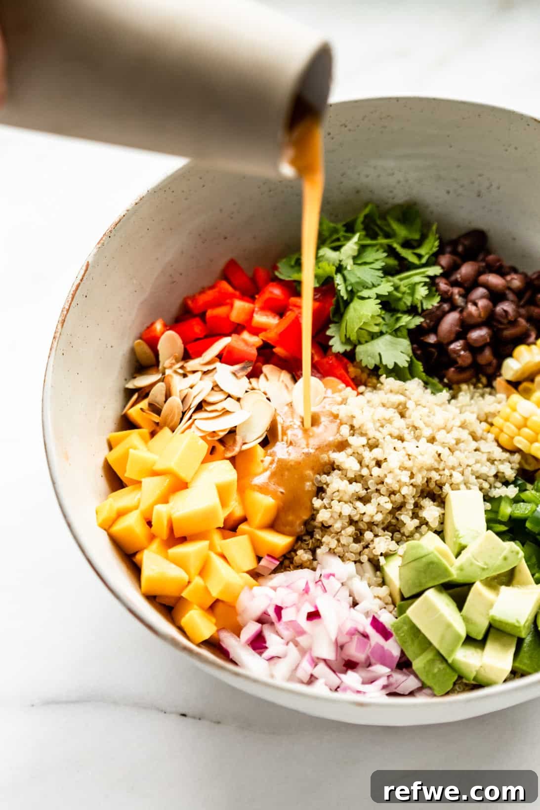 Zesty Southwestern Quinoa Power Bowl 4 A chef's hand gently pouring the vibrant chili lime dressing over the prepared bowl of Southwest Quinoa Salad ingredients.