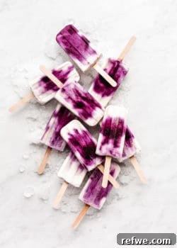 blueberry greek yogurt popsicles stacked on ice on a marble board