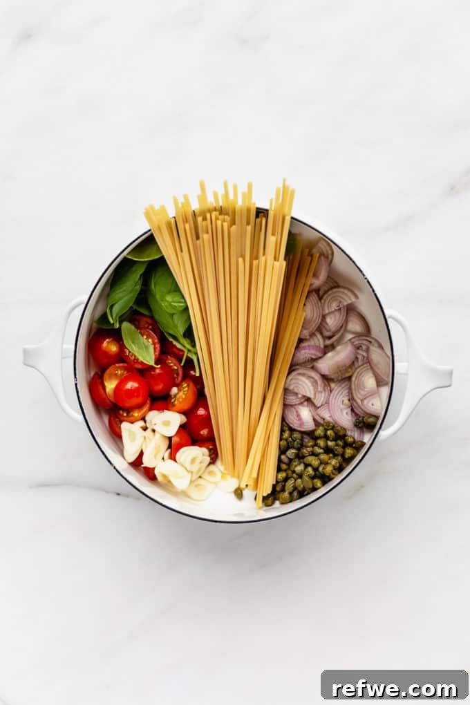 Effortless One-Pan Tomato Basil Pasta 3 A white pot containing uncooked linguine, shallots, capers, garlic, fresh tomatoes, and basil, ready for cooking.