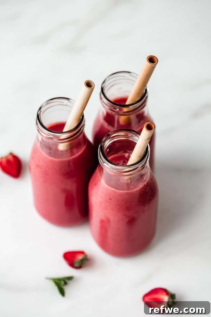 Crimson Chia Berry Delight 6 Three glass jars of red berry smoothies arranged on a sleek marble counter, highlighting their fresh and inviting appearance.