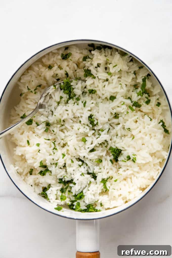 Fluffy white rice in a white pot, mixed with vibrant chopped cilantro and lime juice.