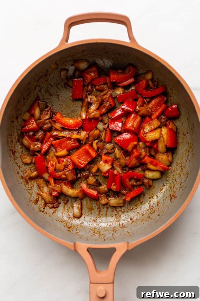 Sautéed onions and red bell peppers glistening in a pink skillet, perfectly cooked and fragrant.