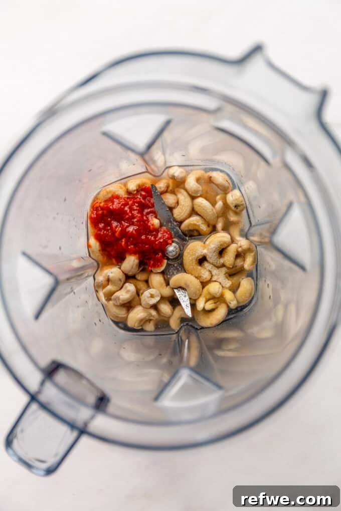 Raw cashews, chipotle peppers in adobo, and various seasonings placed in a blender container, ready to be blended into crema.