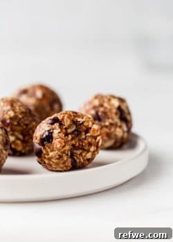 An appetizing trail mix energy ball on a white plate, with a small bite taken out, showcasing the rich texture and delicious ingredients within.