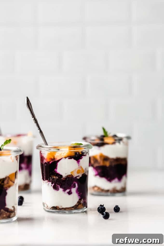 Beautifully layered jars of yogurt and granola parfaits garnished with fresh fruit and mint, ready to be enjoyed.