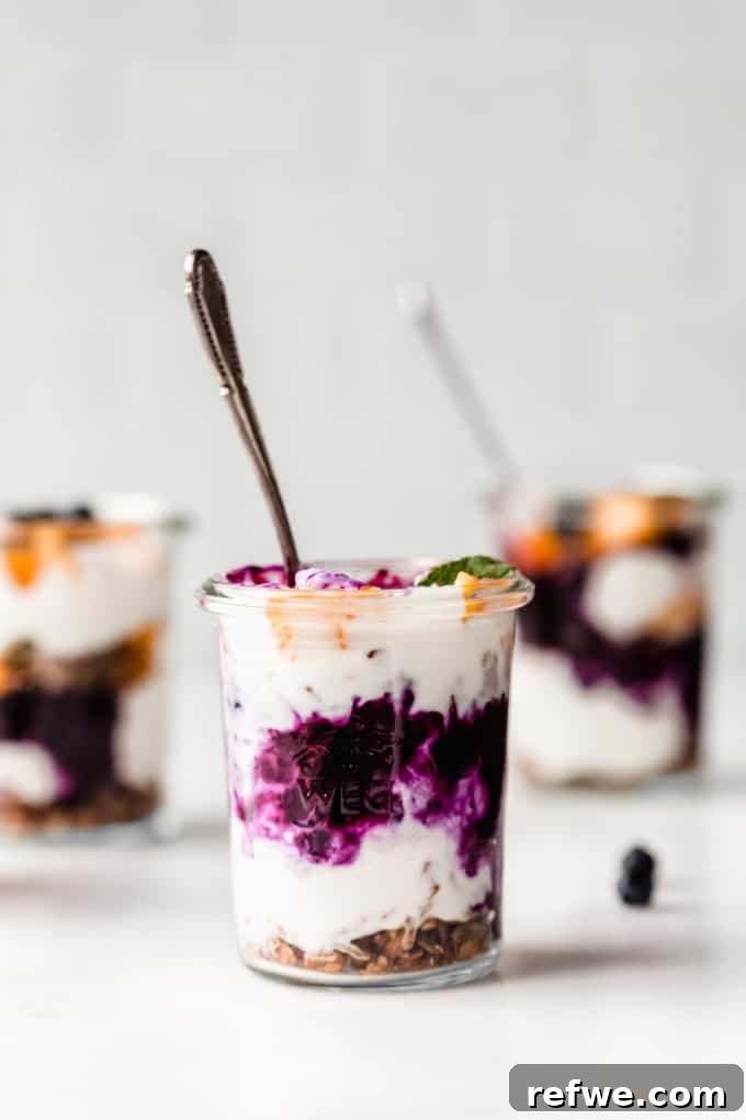 A close-up view of a glass cup partially filled with creamy yogurt and a rich blueberry compote, ready for the next layers of a parfait.