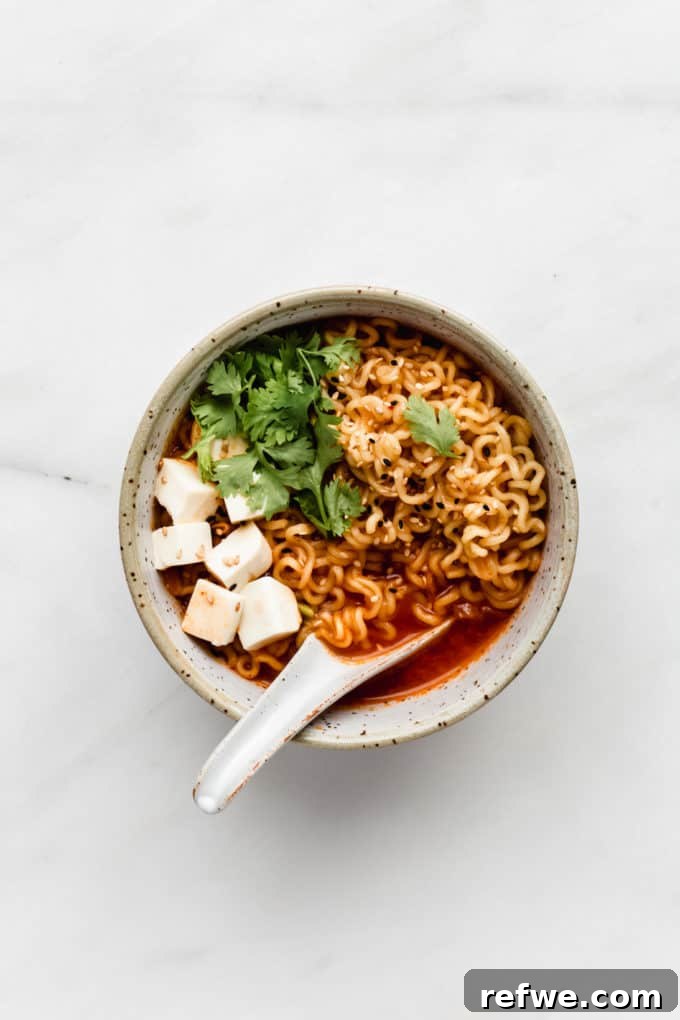 Fiery Kimchi Ramen 3 A close-up of a single bowl of vibrant Kimchi Ramen, featuring soft tofu cubes, spring onions, and a rich, red broth.