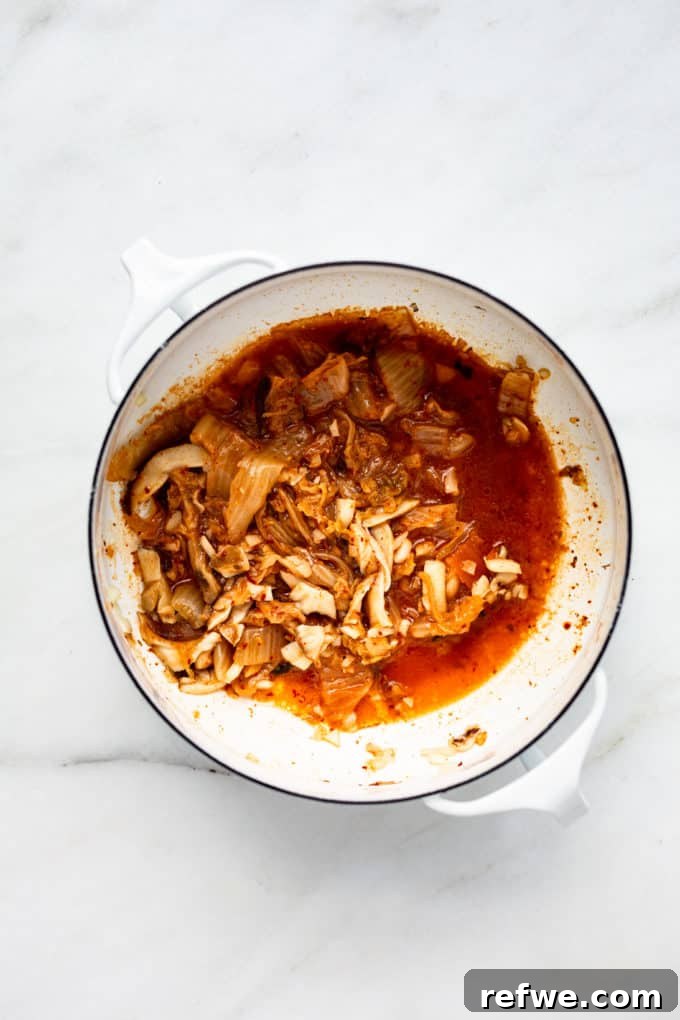 Fiery Kimchi Ramen 5 Kimchi and red curry paste being stirred into the sautéed aromatics in a white pot, creating a rich and fragrant base.