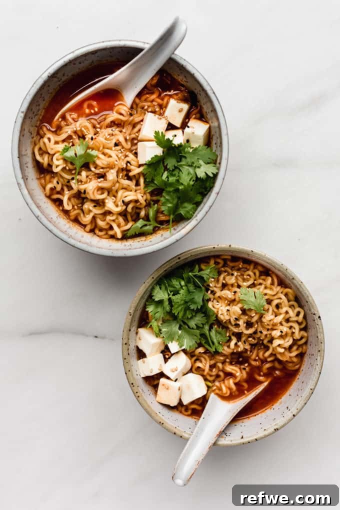 Fiery Kimchi Ramen 7 Two white speckled ceramic bowls of freshly prepared Kimchi Ramen, complete with noodles, tofu, and spoons, ready to be enjoyed.