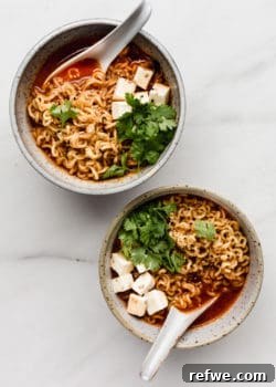 Two white speckled ceramic bowls of kimchi ramen with spoons in them, invitingly presented.