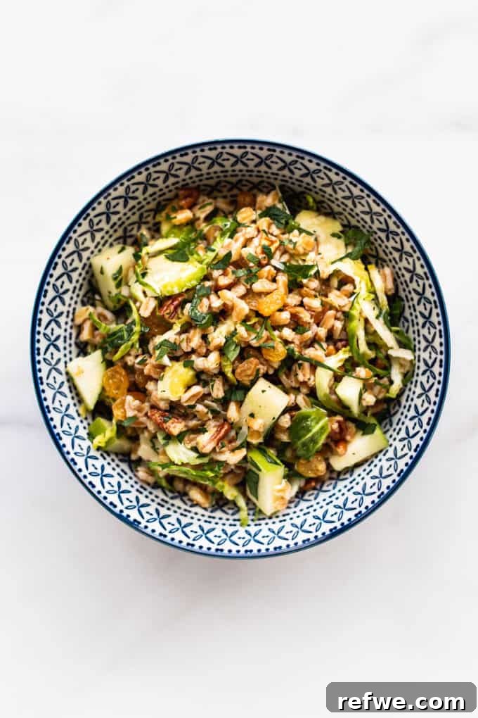 A blue and white bowl filled with a vibrant farro salad, featuring grains, greens, and fruit.