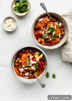 Two bowls of vegetable tagine with two small bowls of almonds and cilantro on the side