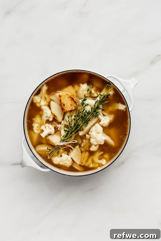 Comforting Slow-Roasted Garlic Soup 4 a white pot with roasted garlic, potatoes, cauliflower and thyme in it