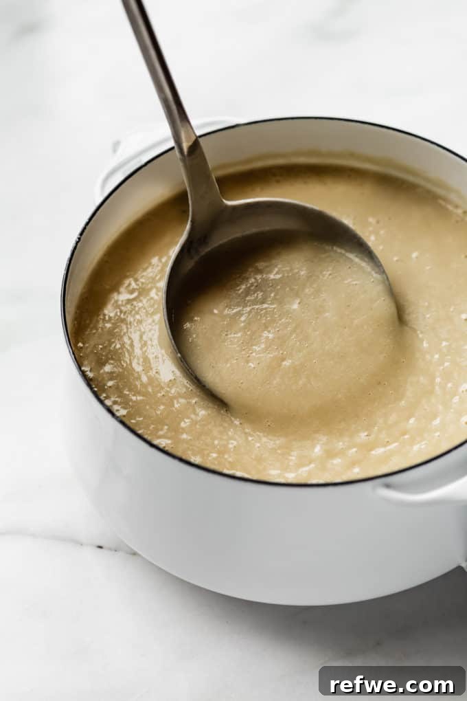 Comforting Slow-Roasted Garlic Soup 6 a ladle scooping garlic soup out of a white pot