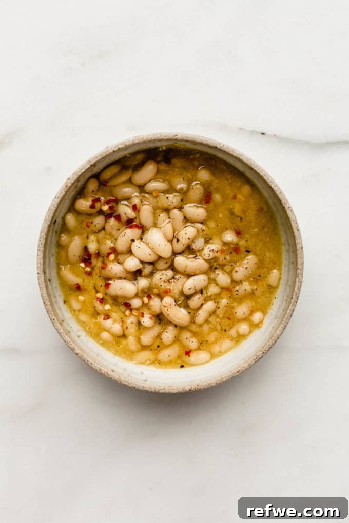 Oven Braised Beans 5 A rustic bowl filled with hearty brothy white beans, garnished with a sprinkle of chili flakes and a drizzle of olive oil, ready to be enjoyed.