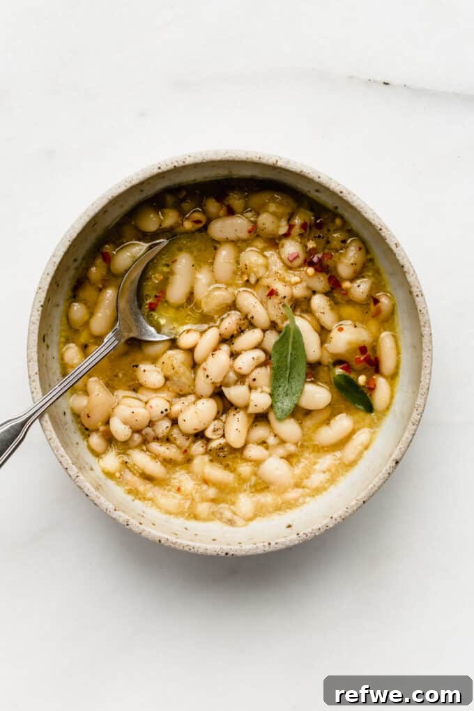 Oven Braised Beans 6 A beautifully presented bowl of creamy cannellini beans swimming in a rich, amber broth, garnished lightly, ready to be enjoyed as a comforting meal.