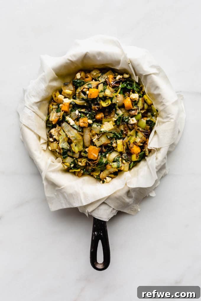 Phyllo dough sheets delicately draped over a cast iron skillet, filled with a colorful medley of sautéed vegetables, ready for folding.