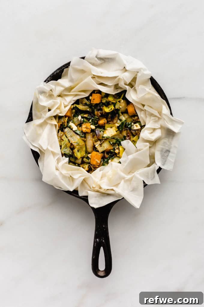 An unbaked veggie phyllo pie nestled in a cast iron skillet, with its delicate phyllo crust neatly folded around the edges.