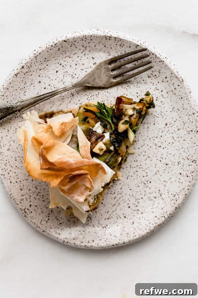 A perfect slice of veggie skillet phyllo pie, showcasing its flaky crust and colorful filling, presented on a white speckled plate with a fork.