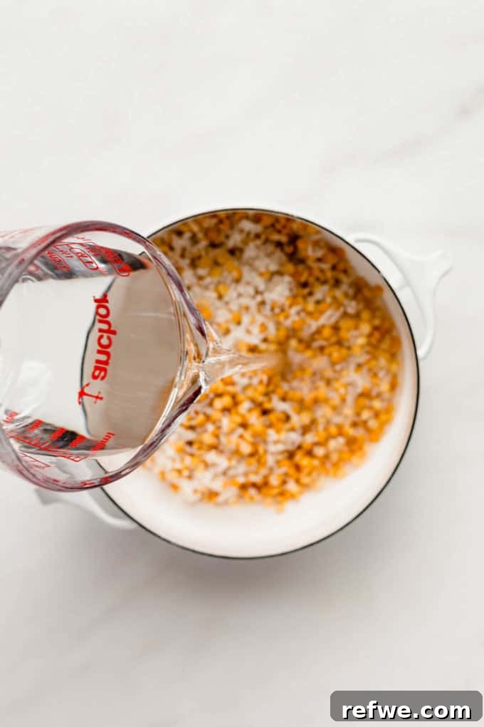 A measuring cup pouring fresh water into a pot of prepared mung beans and rice.