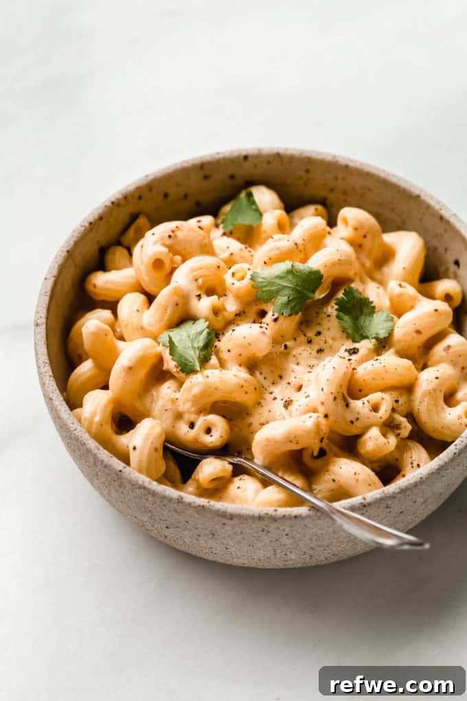 Korean Fusion Vegan Mac and Cheese 7 A close-up of a bowl of creamy vegan kimchi mac and cheese with a spoon, showing off its rich texture