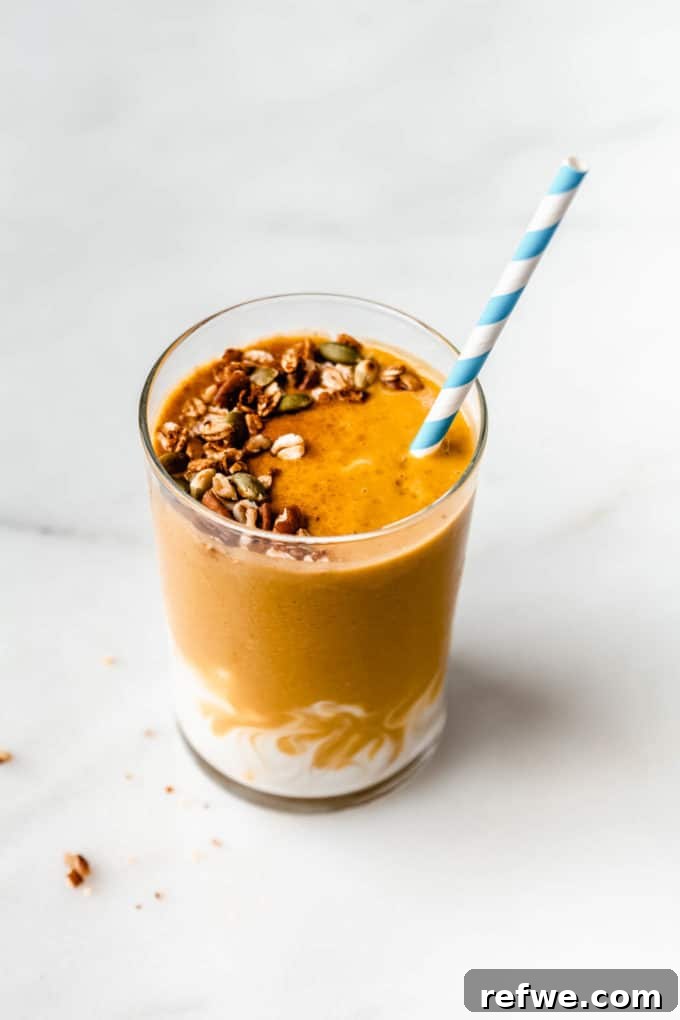 Golden Pumpkin Spice Blend 2 A vibrant orange pumpkin pie smoothie, generously topped with golden granola, features a striped blue and white straw, ready to be enjoyed.